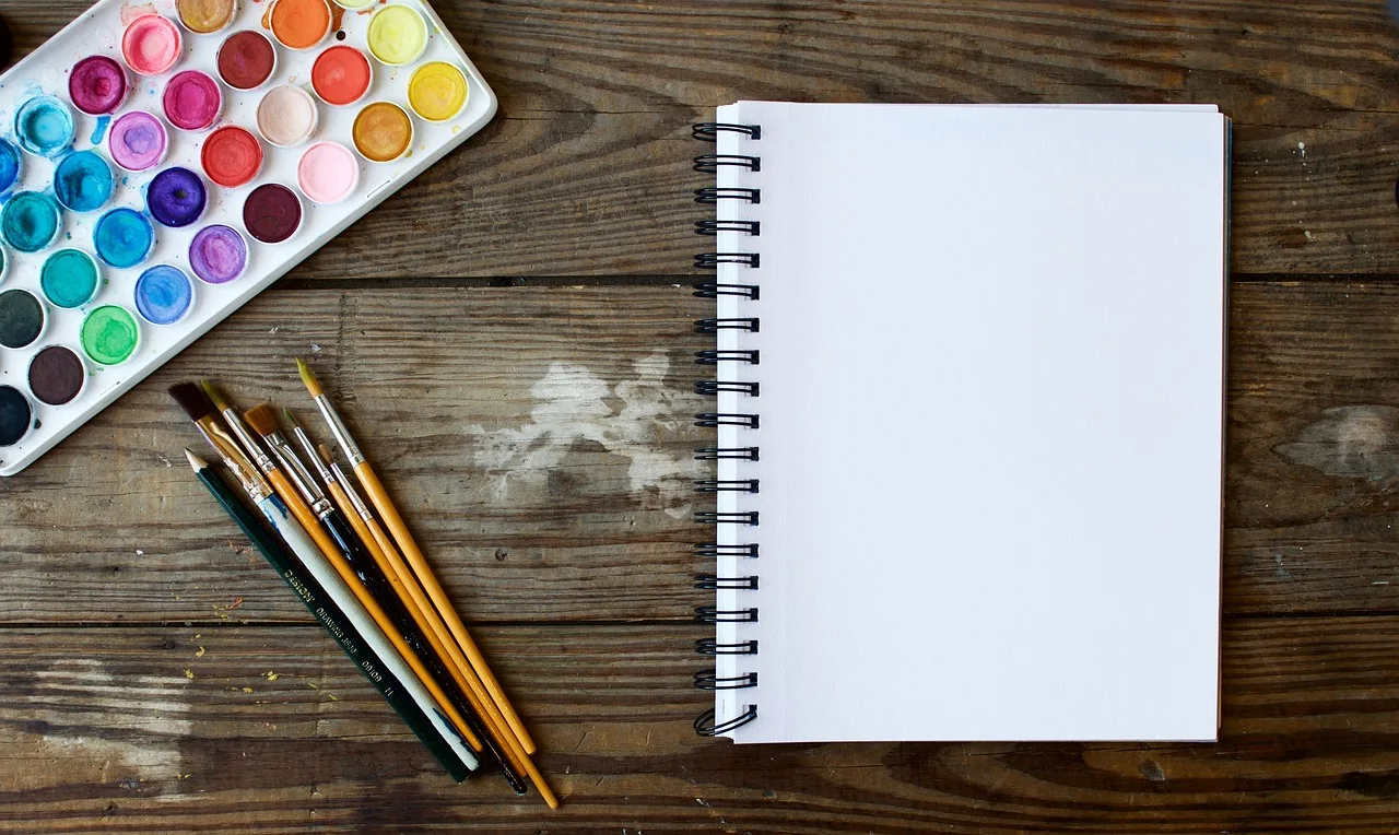 watercolor brushes and paint with empty canvas/notebook